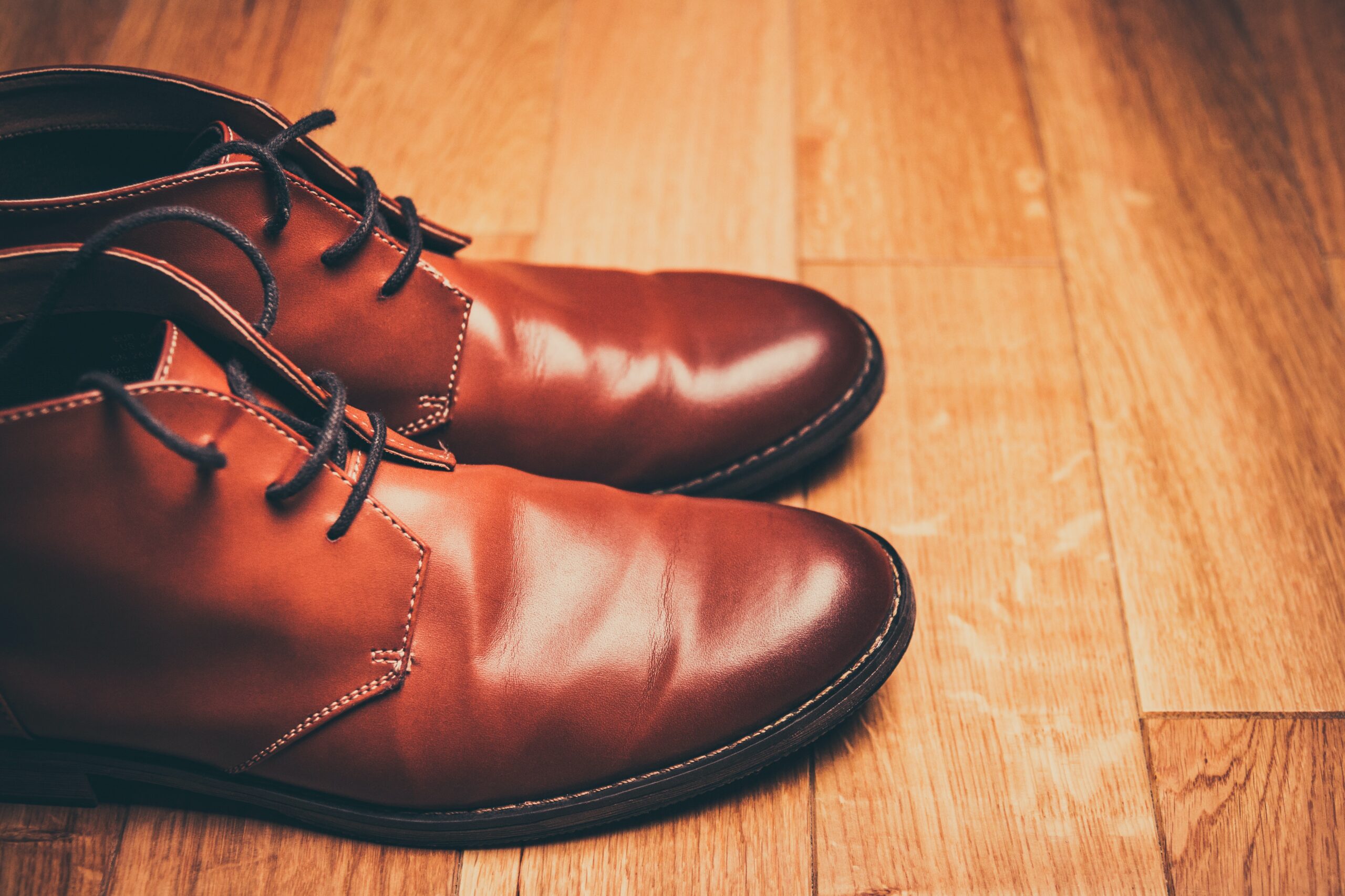Pair of shiny brown leather shoes sit on a wooden floor
