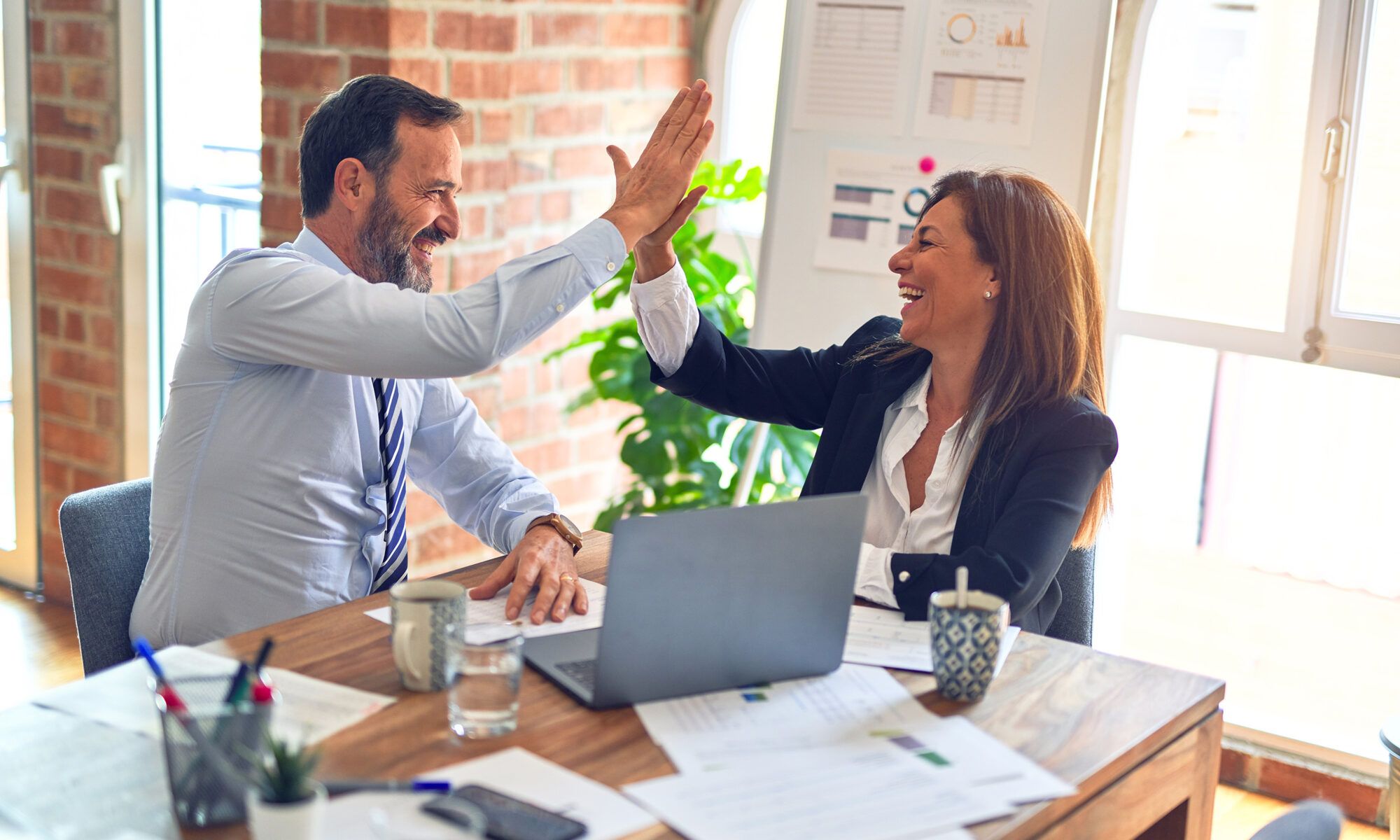 Businesswoman and man high with smiling faces surrounded by business papers and laptop